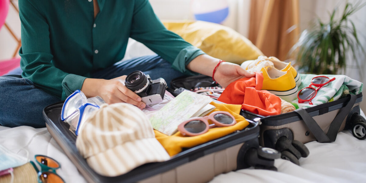 Unrecognizable young woman with suitcase packing for holiday at home, coronavirus concept.